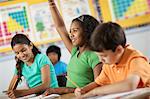 A group of young girls and boys in a classroom, classmates. A girl raising her hand.