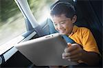A boy travelling in the back seat of a car using a digital tablet.