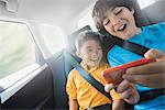 Two children travelling in the back seat of a car sharing a handheld games tablet.