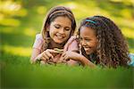 Two girls lying on the grass, one holding a green caterpillar on her finger.