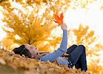 A girl holding up a large orange autumn coloured maple leaf.