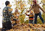 A family, adults and two children playing in autumn leaves.