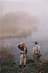 Two people, man and woman standing on the riverbank looking across the water.