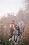 A couple, a man and woman walking along a riverbank with fishing gear.