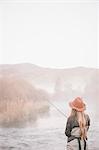 A fisherman, a woman standing on the banks of a river, fly fishing.