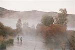 A couple, a man and woman standing in mid stream fly fishing in a river.