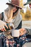 A woman pouring a hot drink from a vacuum flask into a cup on a winter picnic.