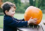 A small boy holding a large orange skinned pumpkin.