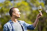 Smiling man looking at a glass of white wine in garden