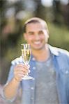 Smiling man looking at a glass of champagne in garden
