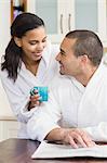 Smiling couple reading newspaper in bath robe and drinking coffee in the kitchen