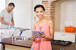 Young man ironing in the kitchen and his girlfriend using tablet at home