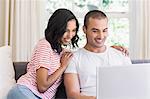 Smiling couple using laptop sitting on the couch at home