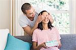 Happy couple offering a gift on the couch at home