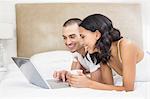 Young couple using laptop in bed at home in the bedroom