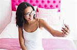 Smiling brunette taking picture with smartphone in pink bedroom