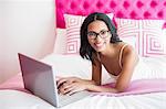 Smiling brunette using laptop in pink bedroom
