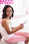 Smiling brunette using tablet in pink bedroom