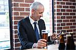 Businessman texting and holding a beer in a pub