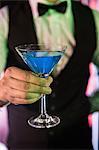 Close-up of bartender serving glass of cocktail at bar counter in bar