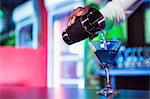 Bartender pouring cocktail from shaker into glass at bar counter in bar