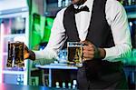 Bartender serving two glasses of beer at bar counter in bar