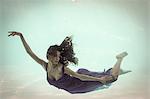 Brunette in evening gown swimming in pool underwater
