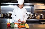 Chef slicing vegetables on wooden board in a commercial kitchen