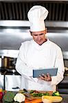 Chef preparing vegetables at counter with tablet in a commercial kitchen