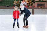 little boy and his mother ice skating together at outdoor skating rink with holiday decorations, having winter vacation fun