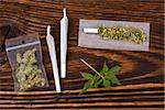 Marijuana background. Cannabis joint, bud in plastic bag and hemp leaves on wooden table. Addictive drug or alternative medicine.