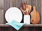 Kitchen cooking utensils on shelf against rustic wooden wall