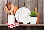 Kitchen cooking utensils on shelf against rustic wooden wall