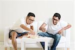 Men talk concept. Two young male friend gathering, chatting and eating at home. Multiracial people friendship.