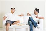 Men talk concept. Two young male friend sitting on sofa and chatting at home. Multiracial people friendship.