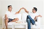 Man sitting on sofa and giving fist bump to friend at home. Multiracial people friendship.