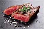 Grilled beef steak with rosemary, salt and pepper on black stone plate