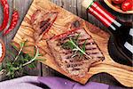 Grilled beef steak with rosemary, salt and pepper and wine bottle on wooden table. Top view