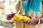 Indian girl with traditional plate of religious offerings and flowers for ear piercing ceremony.