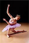 Caucasian teenage girl performing ballet in studio, with a wooden laminate floor and black background