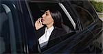 Serious young female executive with button collar on phone and sitting in rear seat of limousine with window down