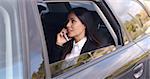 Beautiful young business woman with long hair in conversation on phone while sitting in rear seat of limousine with window down