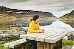 Beautiful woman resting close to a beautiful lake and drinkign a tea