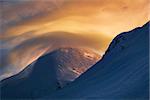 Enchanting color spectacle in winter mountains - red-ene-yellow clouds dance round the mount. Dark snow surface contrasts with bright clouds.