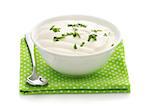 Natural sour cream in a white bowl with chopped potherbs, spoon, green napkin isolated on a white background close up