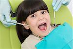 Little brunette lady having her teeth examined by professional dentist. Lady sitting with her mouth opened.