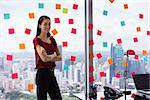 Portrait of proud assistant with arms crossed.The woman stands in office at high floor, against window full of adhesive notes with tasks