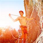 attractive muscular male climber with the rope under the cliff against blue sky