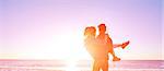 happy attractive man and woman walking on the sunny beach over the blue sky. man holding a woman on the hands.