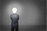 Man in a business suit stands with his back, before him empty concrete wall. Instead of head businessman lighting bulb.